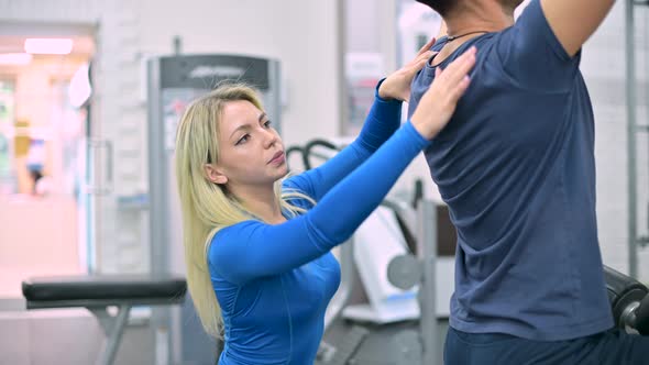 Young woman trainer monitors the correctness of the exercise by the man alt
