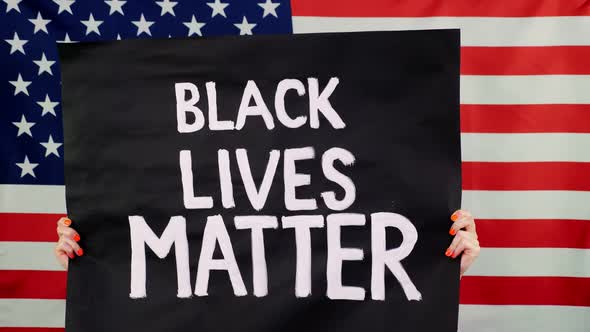 Protester Holds a Banner with a Slogan - Black Lives Matter - Against Background of the USA Flag alt