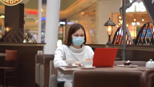 Woman in Protective Mask Working on Laptop in a Shopping Center in a Cafe