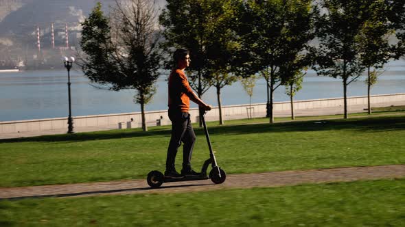 A Man is Riding Electric Scooter in City Park Area at Sunny Morning