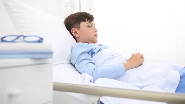 Child in hospital lying in bed bored taking a book to read