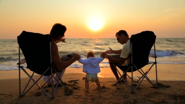 Two Men In Outdoor Chairs And Baby On The Beach