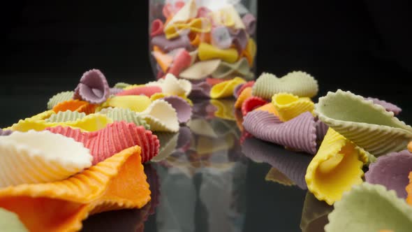 Creative Multicolored Pasta Farfalle on a Black Background in Perspective with Packaging in