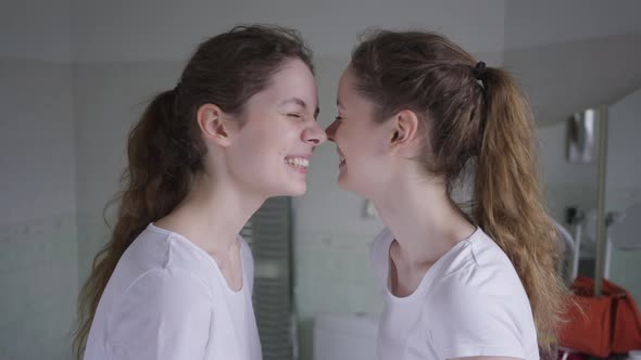 Side View Laughing Cheerful Beautiful Slim Twin Sisters Looking at Each Other Rubbing Noses alt