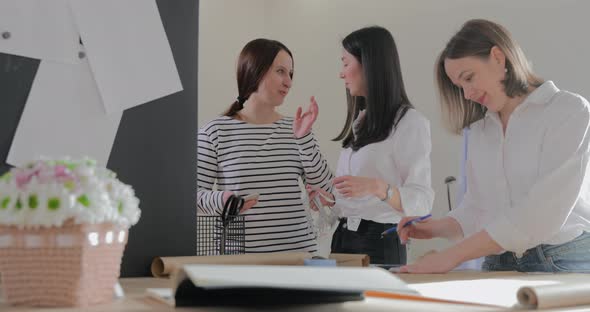 Three Fashion Designer Works at a Table and Discuss About Something Curves and a Pattern Scissors alt