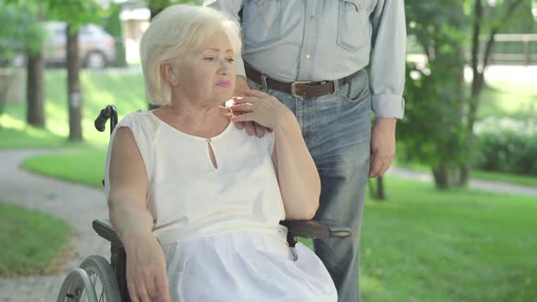 Unrecognizable Man Putting Hand on Shoulder of Sad Paraplegic Woman Sitting in Wheelchair. Portrait alt