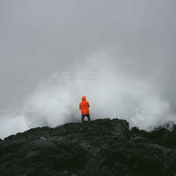 Man facing fierce wave on volcanic rocks.