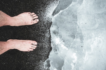 Bare feet on the Black sands with an Iceberg