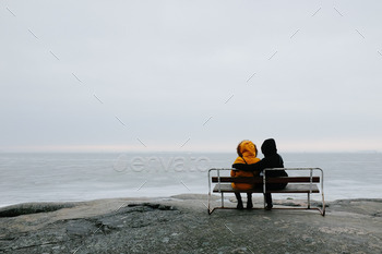 Two people cuddling on a bench facing a cold, frozen sea.
