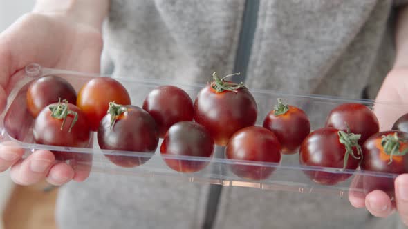 Woman Shows Organic Black Cocktail Tomatoes in a Plastic Box