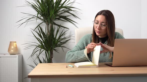 Young Entrepreneur Woman with Eyeglasses Working on Laptop and Writing Notes on Notebook in a Cozy alt