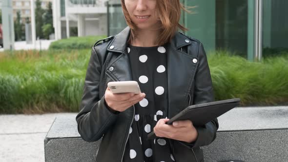 Modern Business Woman Uses a Mobile Phone and Holding a Tablet in Her Hands Waiting for a Client on alt
