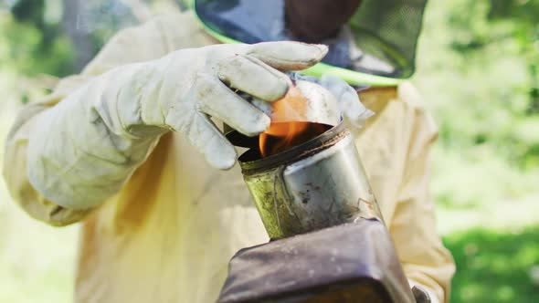 Caucasian male beekeeper in protective clothing preparing smoker alt