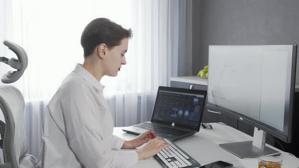 Lovely Young Woman Smiling To the Camera While Working on Her Two Computers alt