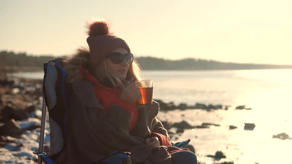 Female Drinking Hot Tea Or Coffee From Mug. Woman Warming Hands Steaming Cup Of Mate Tea. alt