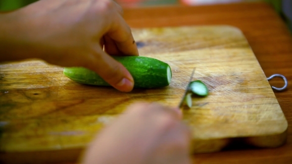 Female Hands Cutting Cucumber On Wooden Board