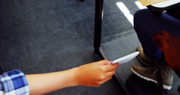School students passing a chit in a secretive way inside the classroom alt