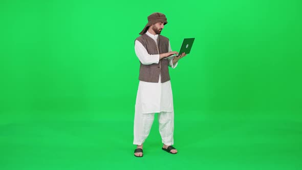 A Man of Arab Appearance in Traditional Clothes Uses a Laptop to Surf the Internet While Stands alt