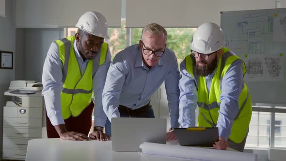 Engineers and Contractor Brainstorm in Office with Laptop and Clipboard alt