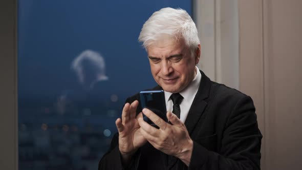 Cheerful Elderly Businessman in Blazer with Mobile Phone Texting and Smiling alt