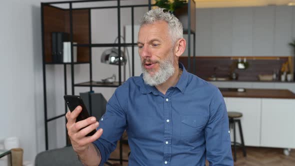 Grey Haired Businessman in Smart Casual Wear is Using Smartphone for Video Connection alt