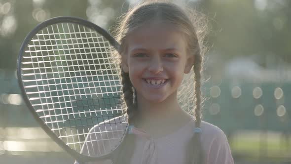Portrait Cute Little Smiling Girl with Pigtails and a Tennis Racket on Her Shoulder alt