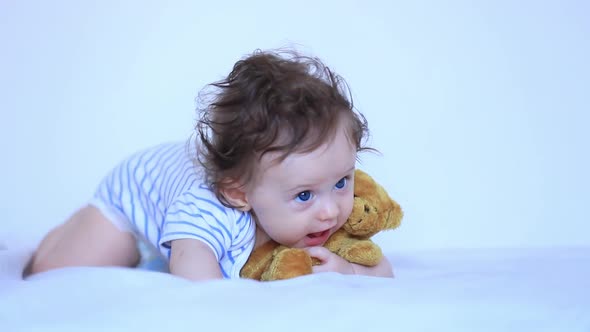 Little child boy with blue eyes and teddy bear in white bed