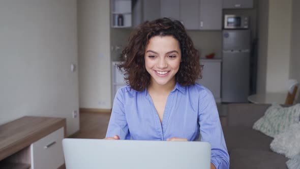 Happy Latin Young Woman with Curly Hair Talking with Friends on Laptop Computer alt