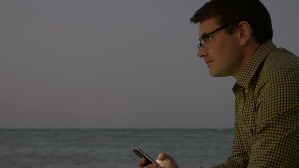 Young Man Using Smart Phone By Sea In The Evening Young Man Using Smart Phone By Sea In The Evening