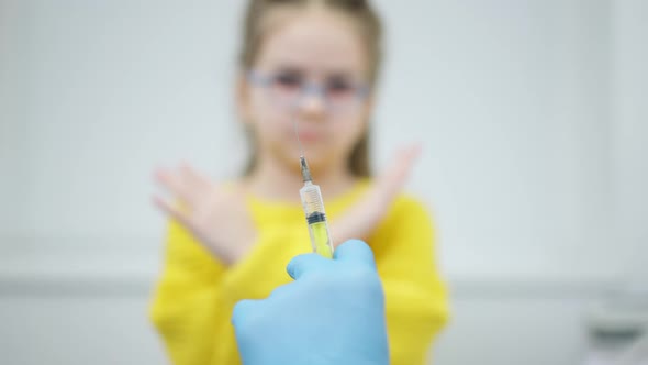 Closeup of Pediatrician Hand Holding Syringe with Covid Vaccine and Blurred Caucasian Little Girl alt