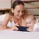 Young Mother with Newborn Daughter Watching Cartoons Through Smartphone Online Application - VideoHive Item for Sale