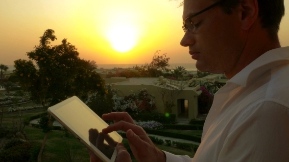Businessman On Vacation Using Touch Pad At Sunset Businessman On Vacation Using Touch Pad At Sunset
