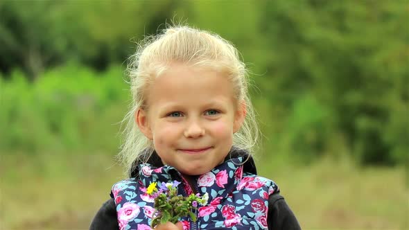 A portrait of a cute little girl. Beautiful Little girl enjoys the smell of flowers in the meadow.