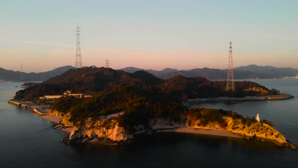 Backwards Aerial Drone movement over island with lighthouse and powerlines at sunset alt