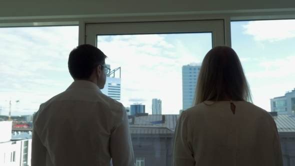 Two Businesspeople Go To Window In The Office Two Businesspeople Go To Window In The Office
