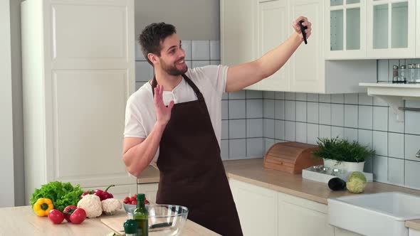 Man in an Apron Takes a Selfie While Standing in the Kitchen Before Preparing a Vegan Meal alt