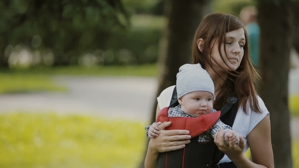 A Young Mother Carrying Her Baby In a Baby Carrier A Young Mother Carrying Her Baby In a Baby Carrier