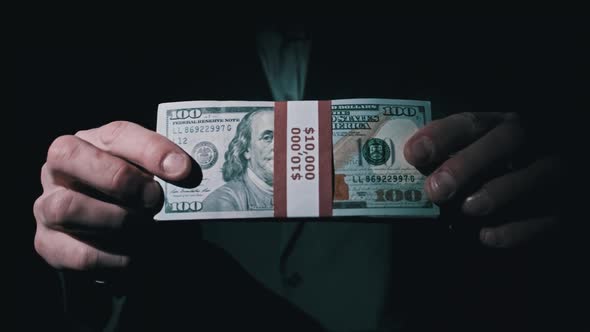 Businessman in Suit Shows Stack of 10000 American Dollars on Black Background alt