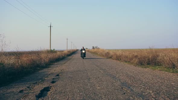 Stylish Cool Young Man in Sunglasses and Leather Jacket Approaching While Riding a Motorcycle on a alt