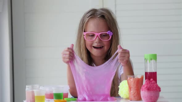 Little girl stretching pink slime to the sides.