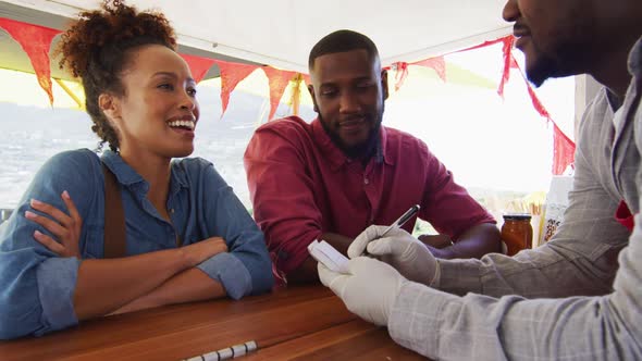 African american man wearing apron taking order from a couple at the food truck alt