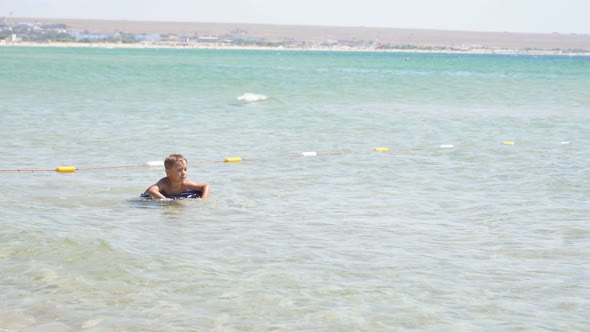 Happy Child Learns to Swim in the Sea on an Inflatable Pillow