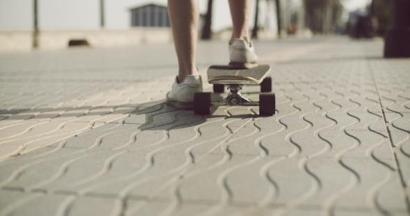 Man Pushing a Skateboard Along a Textured Sidewalk Man Pushing a Skateboard Along a Textured Sidewalk