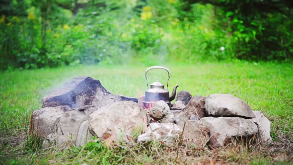 Man Placing A Kettle On A Camp Fire