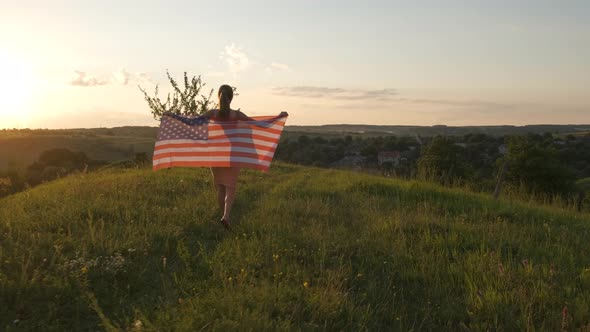 Happy Young Woman Posing with USA National Flag Standing Outdoors at Sunset alt