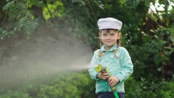 Funny Little Girl in Hat Playing with Garden Hose in Sunny Backyard