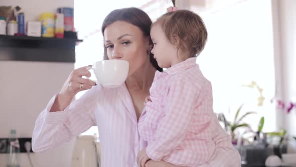 Mother with Daughter Standing at Kitchen and Drinking Coffee