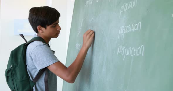 Schoolboy writing on green chalkboard in classroom alt