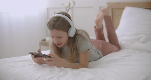School Girl Is Using App in Smartphone, Lying in Bedroom and Talking, Leisure of Children in Weekend alt