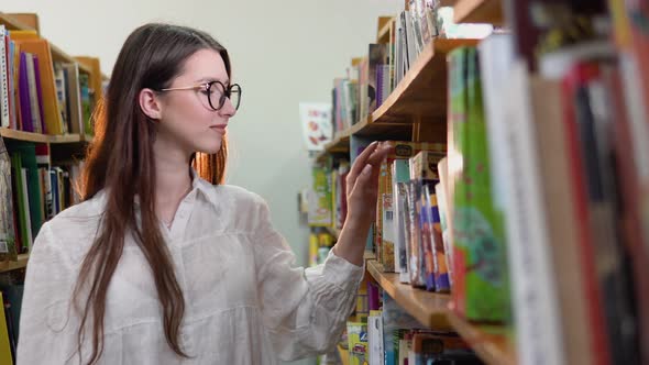 A University Student is Looking for a Book on Bookshelves in the Library alt